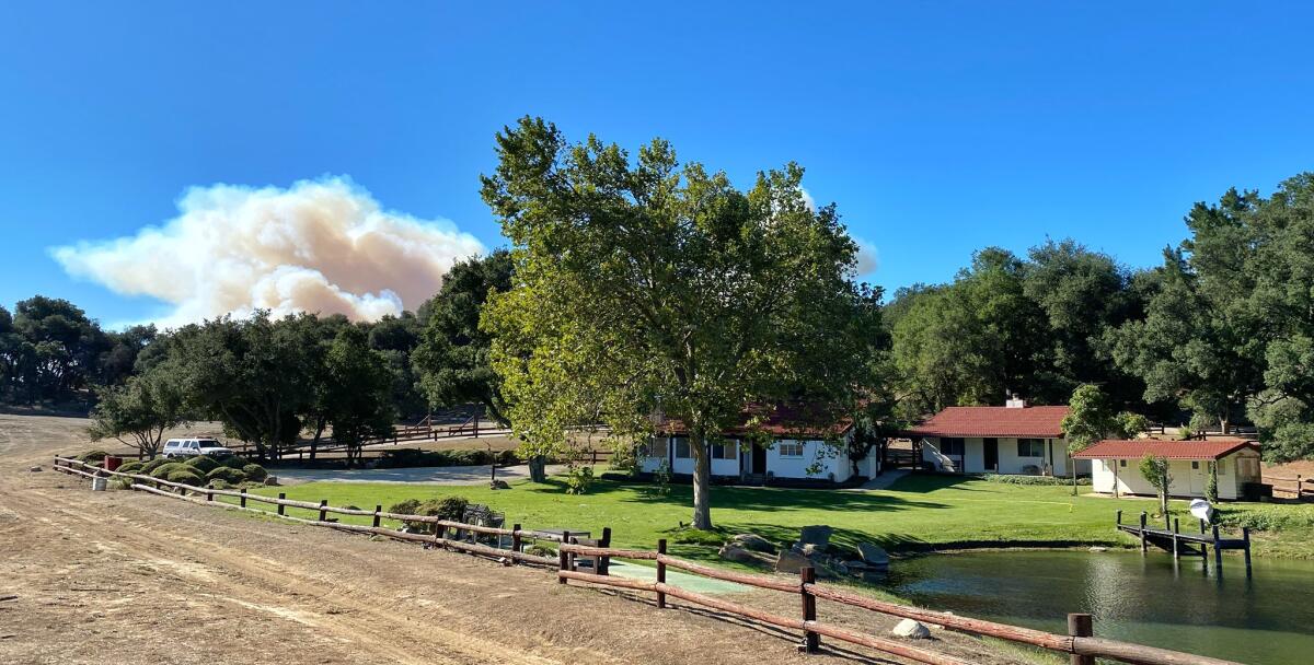 Smoke rises in the background behind a ranch house