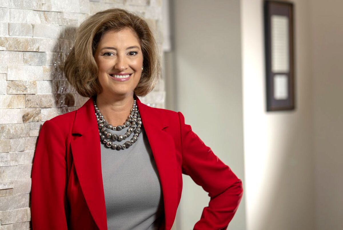 A woman, in tailored jacket and bead necklace, poses for a portrait.