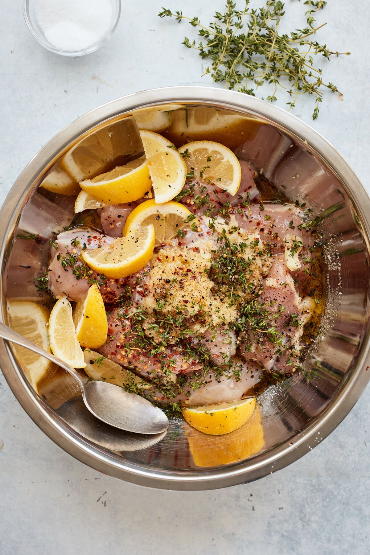 Raw chicken pieces are tossed in a large bowl with lemon, herbs and aromatics.