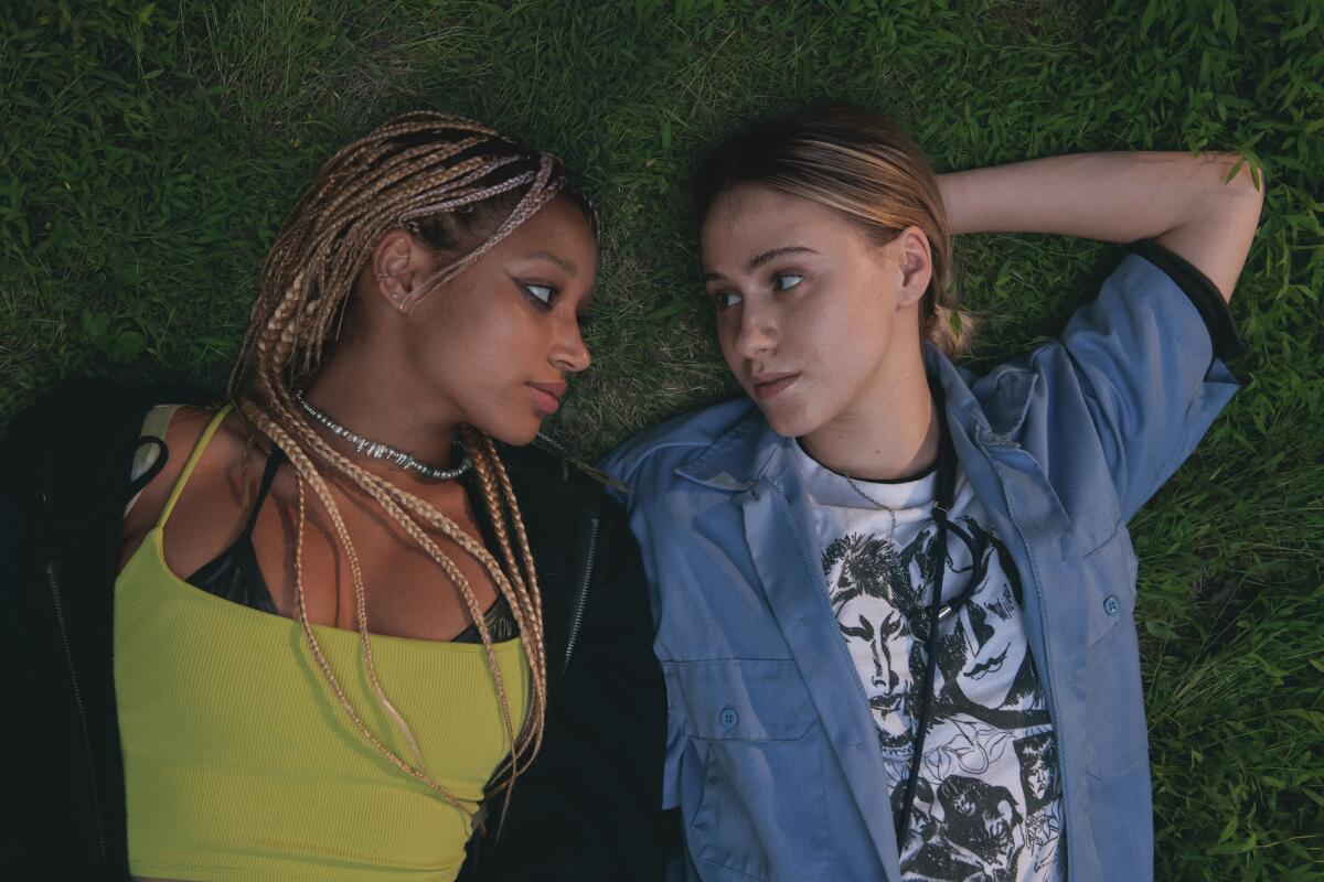 Two young women lie on the grass together.