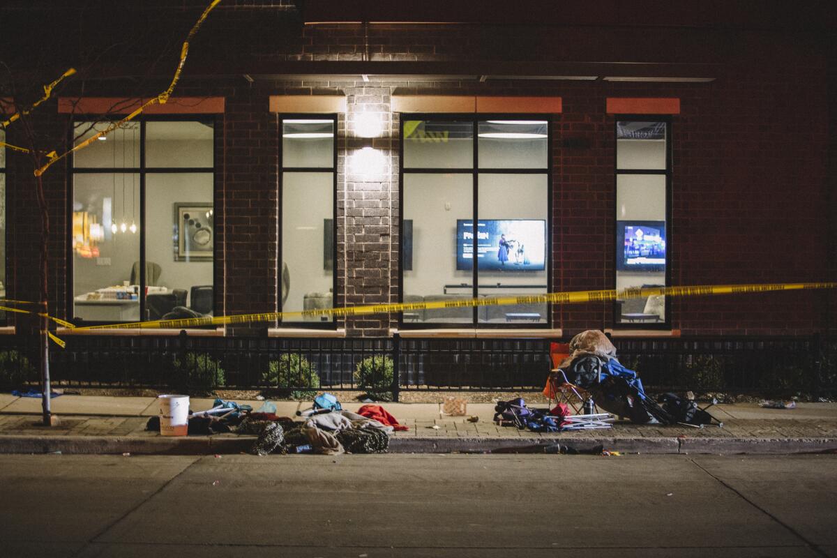 Clothes, trash and folding chairs on a sidewalk behind crime scene tape