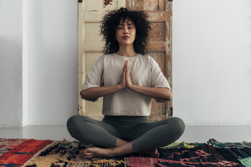 Multiracial young woman meditating with hands in prayer at home. Meditation concept. Spirituality concept.