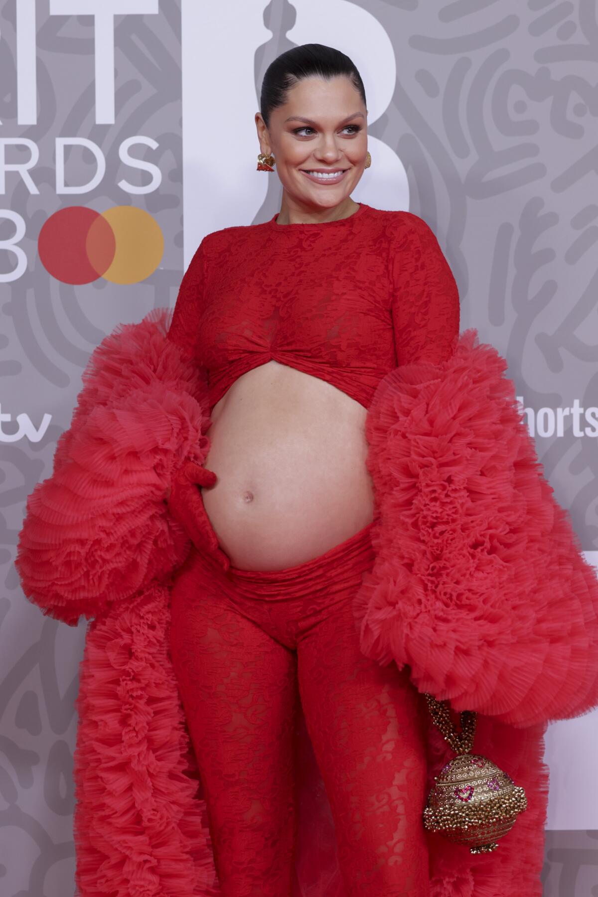 Jessie J poses in a lacy red ensemble with a fluffy red coat and a cutout revealing her pregnant belly 