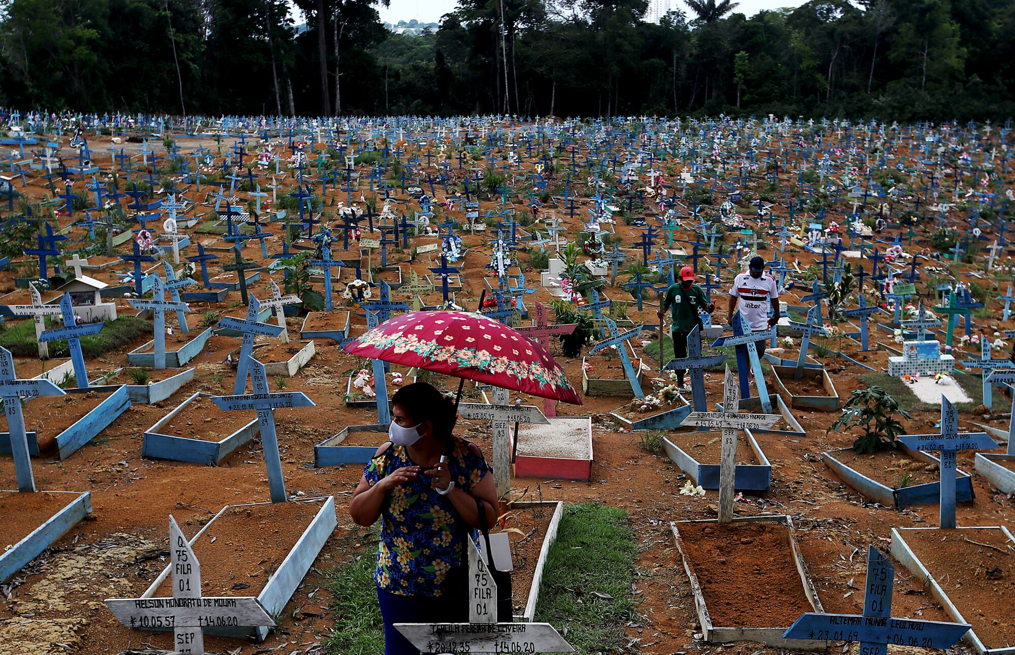 A large graveyard of crosses over gravesites with three people among them