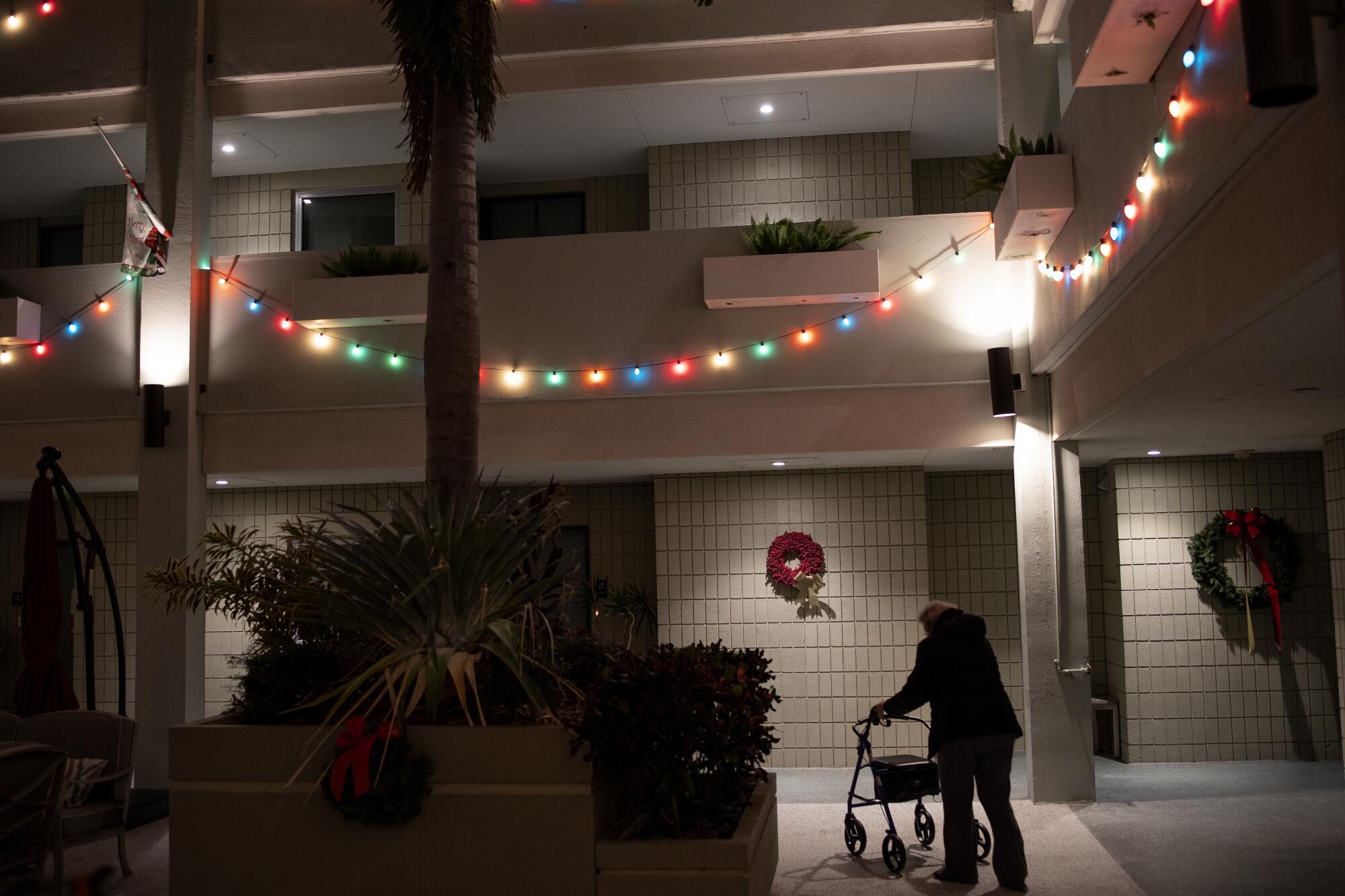 A silhouetted woman uses a walker in an apartment complex decorated with Christmas lights.