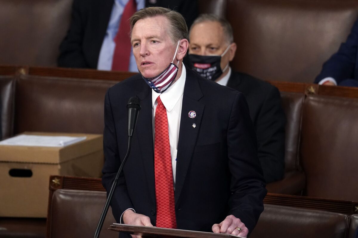 Rep. Paul Gosar stands at a microphone with a U.S. flag mask pulled under his chin.