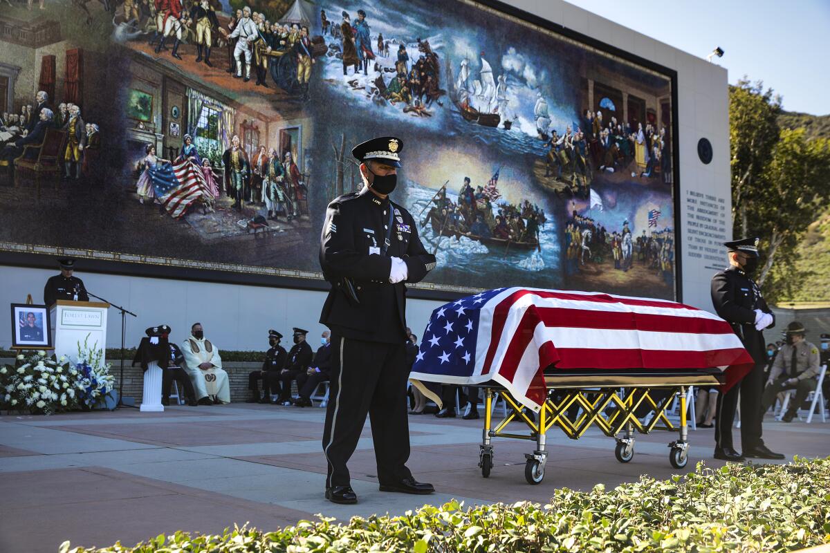A police officer stands next to a casket covered with the U.S. flag.