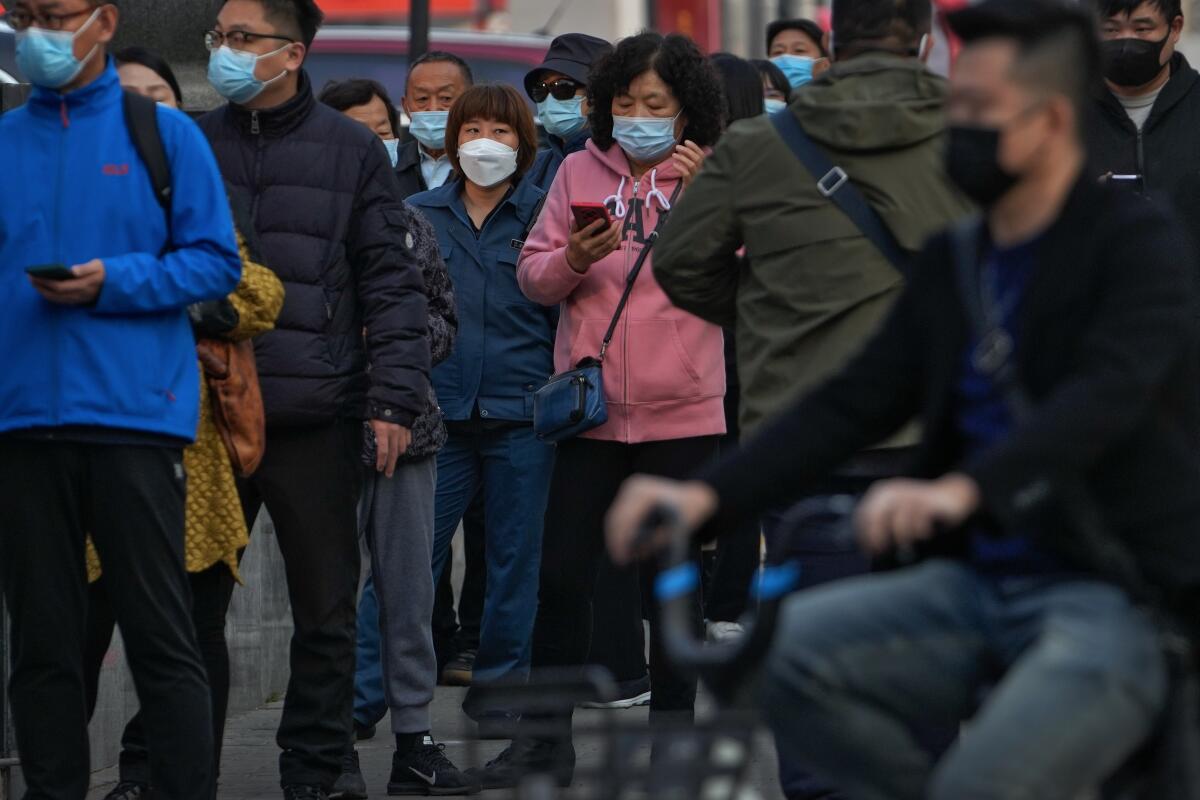 Residentes con mascarilla esperan en fila para someterse a una prueba rutinaria de detección del COVID-19, en Beijing