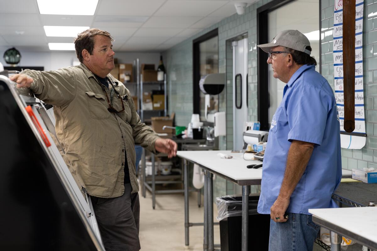 Two men talk behind the counter of the TunaVille market.