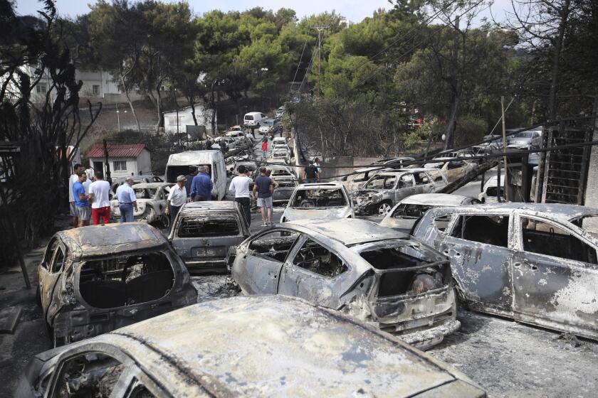 FILE - People stand amid the charred remains of burned-out cars in Mati east of Athens, Greece, Tuesday, July 24, 2018. A court on Monday, April 29, 2024, has convicted five former Fire Service and disaster response officials over a 2018 wildfire outside Athens that killed more than 100 people. (AP Photo/Thanassis Stavrakis, File)
