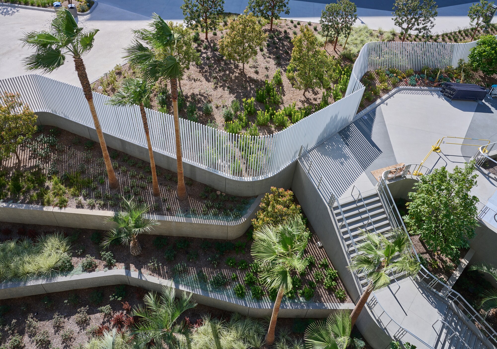 An overhead view shows zigzagging garden terraces pierced by an undulating fence and a staircase.