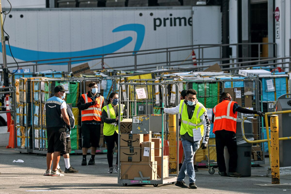 Workers in reflective vests and masks move boxes at an Amazon facility.