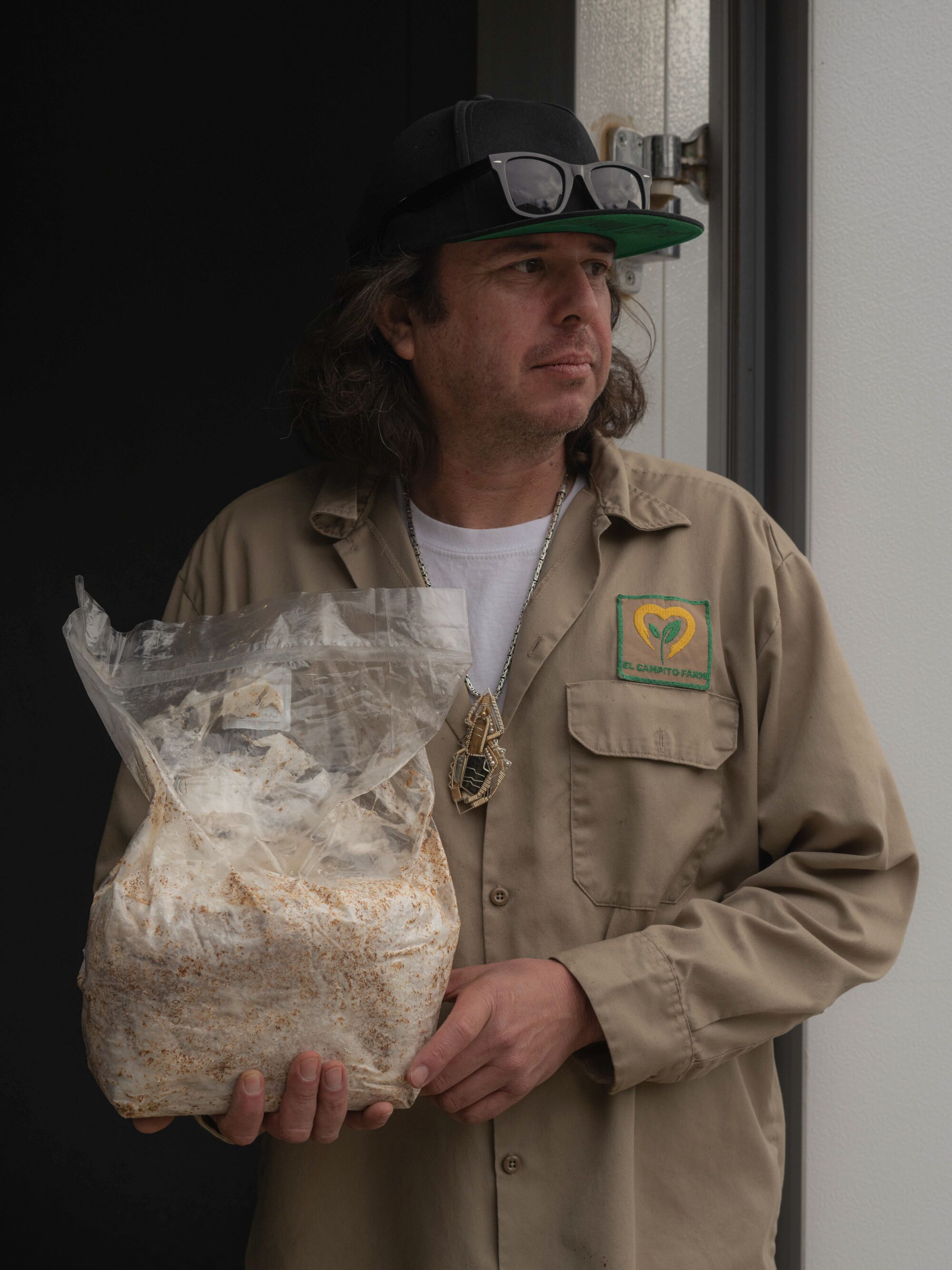 A man in sunglasses and a hat holding a big bag of mushrooms.
