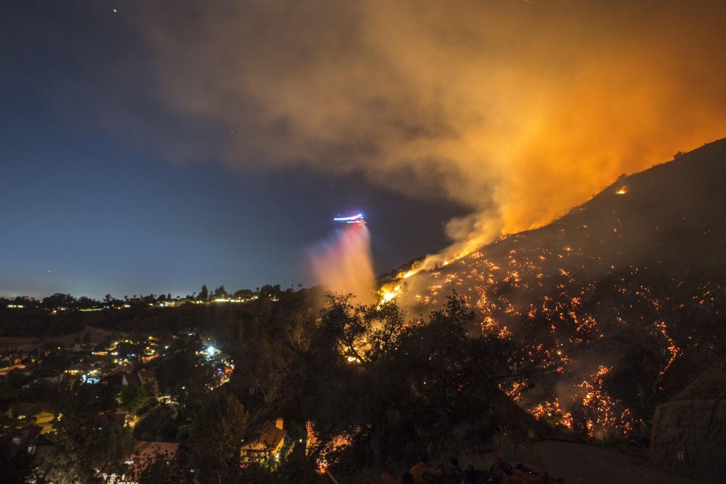 The Fish fire burns near homes in Bradbury on Monday evening as a Los Angeles County fire helicopter makes a nighttime water drop in a long-exposure image.