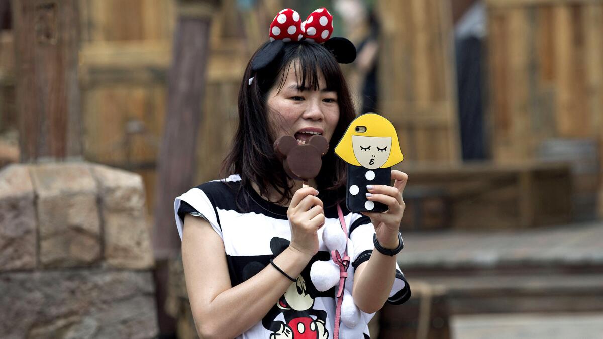 The Disney fandom is international. A visitor snaps a selfie while wearing Minnie Mouse ears and a Mickey Mouse T-shirt, eating a mouse-ear-shaped ice cream bar at the Disney Resort in Shanghai, which opened 2015.