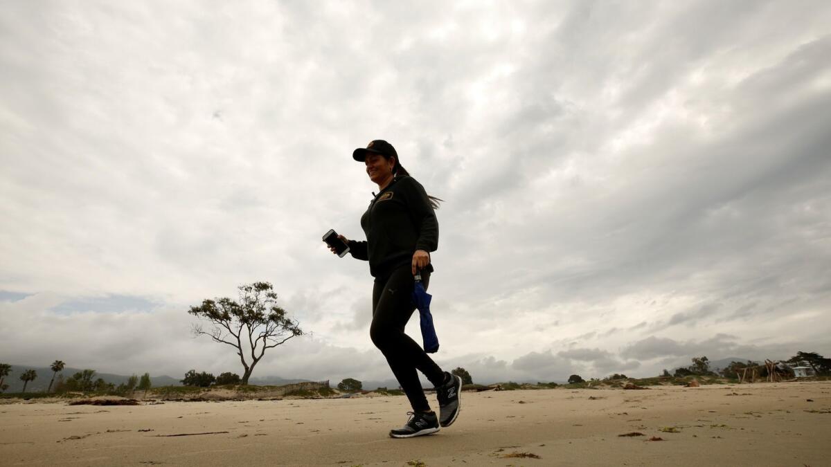 Lucy Macias, vacationing from Mexico, jogs with her umbrella Monday morning at Carpinteria State Beach between rain squalls as a weather system moved through the Southland.