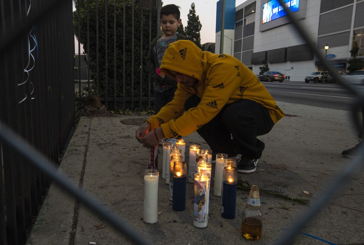 A man in a hoodie kneels at a makeshift memorial, with a boy beside him.