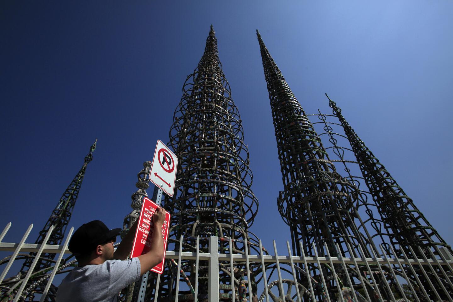 Street artist Jason Shelowitz (a.k.a. Jay Shells) installs a sign at Watts Towers featuring rap lyrics by Crooked I: "Got street power from the Watts Towers to Howard Hughes. How would you become me I don't Do what you cowards do."