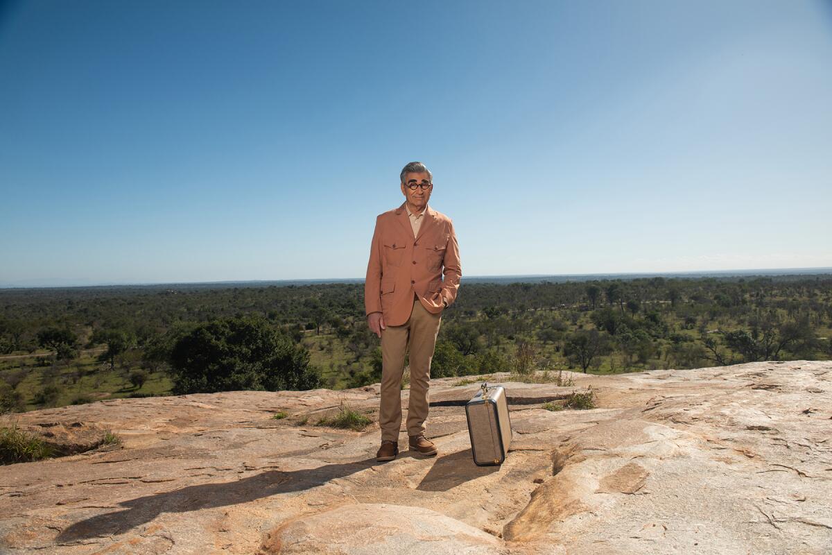 Eugene Levy standing alone in a remote location with a suitcase "The Reluctant Traveler" on Apple TV+.
