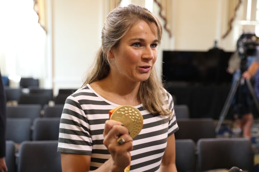 Becca Meyers shows reporters one of her gold medals that she won in the 2016 Paralympics after a news conference on Monday, July 26, 2021 in Annapolis, Md. Meyers, a Maryland native, received a certificate from Gov. Larry Hogan recognizing her "bravery for highlighting the issue of inequality and access for people with disabilities." Meyers withdrew from this year's Tokyo games because she could not bring her mother with her as her personal care assistant. (AP Photo/Brian Witte)