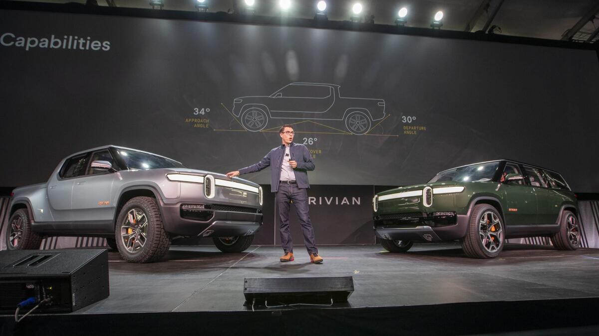 R.J. Scaringe, founder and CEO of Rivian Automotive, shows the company's R1T electric truck, left, and R1S SUV during the L.A. Auto Show in November.