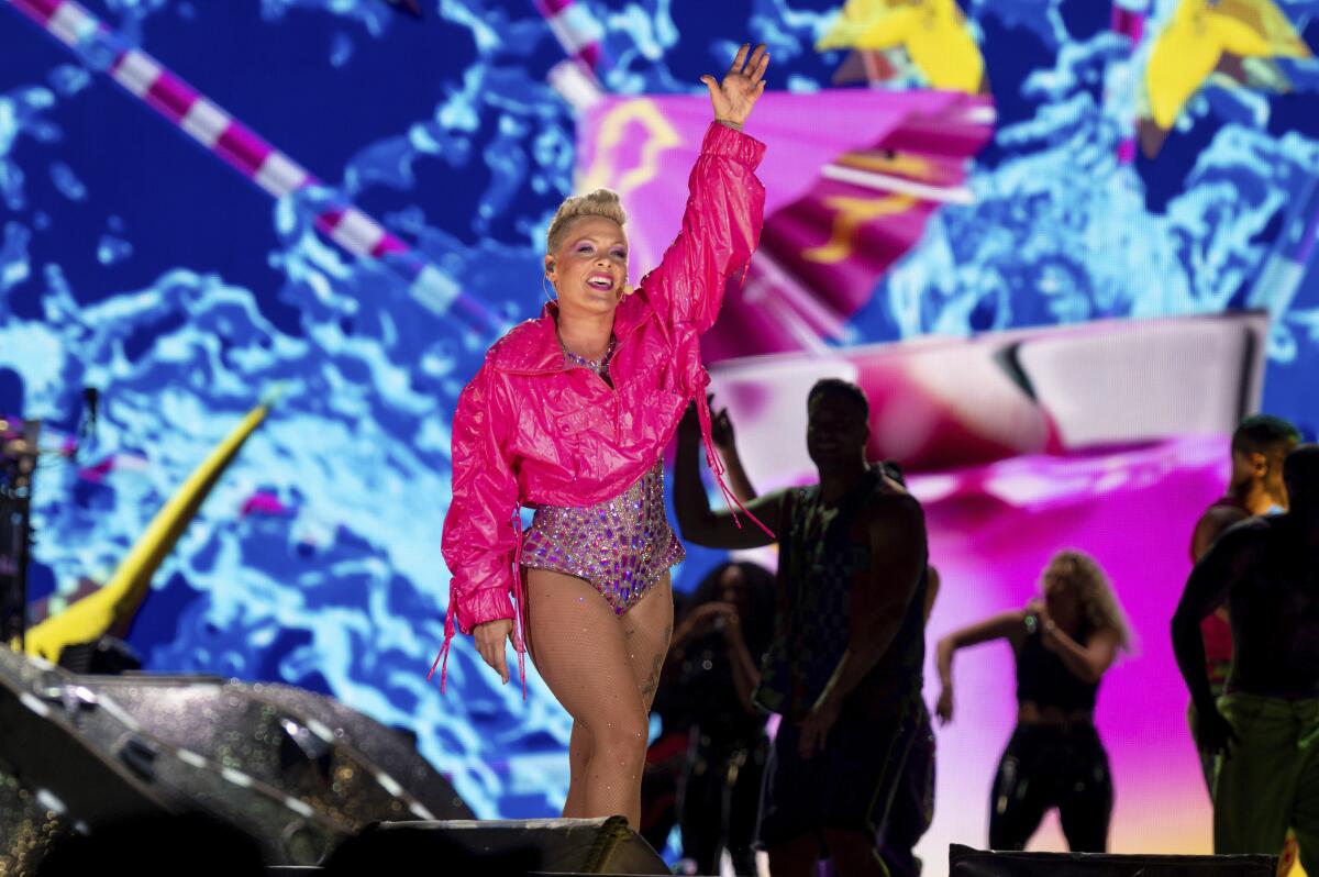 Singer Pink in a pink jacket and a purple bedazzled leotard performing on a stage and holding her left hand up