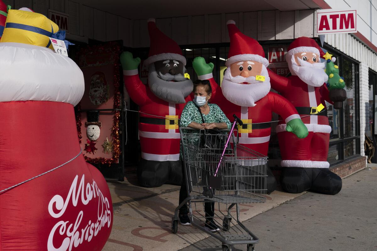 A shopper wearing a face mask pushes an empty cart past inflatable Santa Clauses