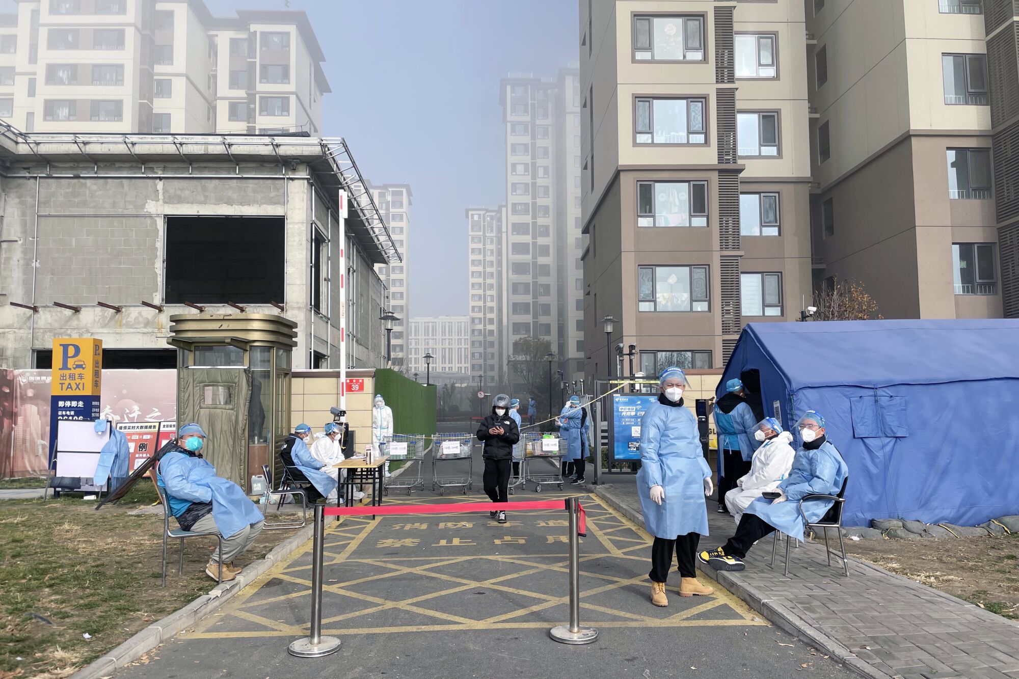 Maskeli, önlüklü sağlık çalışanları bir bariyerin arkasında duruyor.