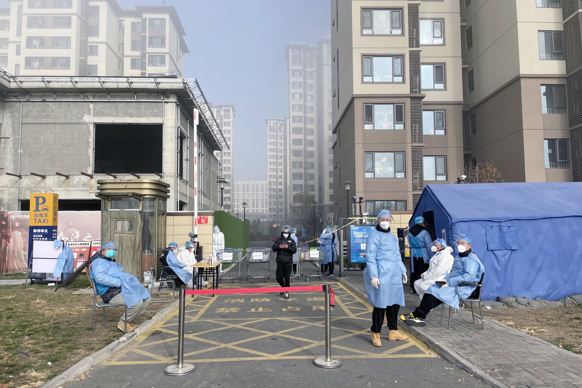 Masked, gowned health workers stand behind a barrier.