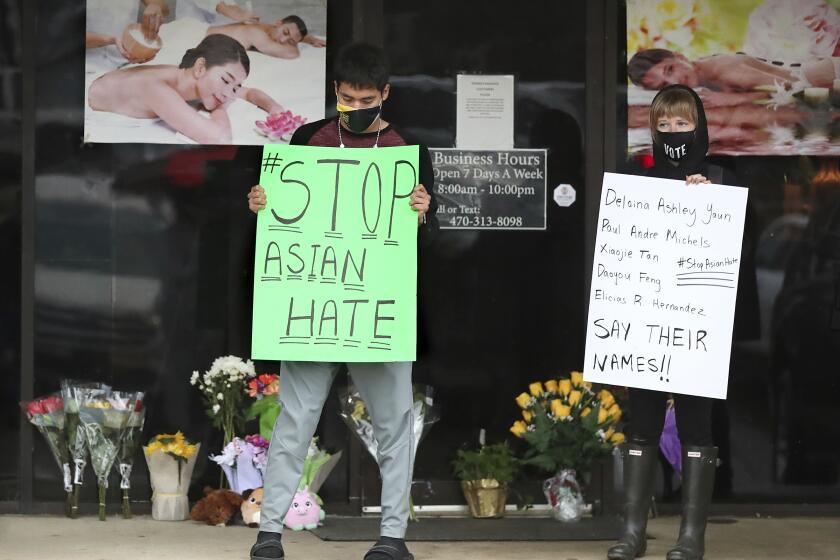 After dropping off flowers Jesus Estrella, left, and Shelby stand in support of the Asian and Hispanic community outside Young's Asian Massage Wednesday, March 17, 2021, in Acworth, Ga. Asian Americans, already worn down by a year of racist attacks fueled by the pandemic, are reeling but trying to find a path forward in the wake of the horrific shootings at three Atlanta-area massage businesses that left eight people dead, most of them Asian women. (Curtis Compton /Atlanta Journal-Constitution via AP)