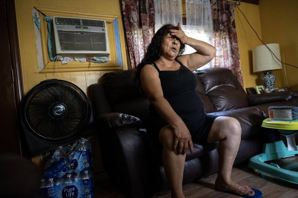 A woman sits on a couch with her hand on her forehead