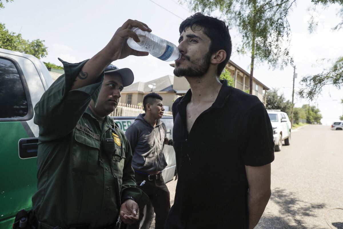 Border Patrol paramedic Roy Ramirez gives water to detainee Juan Carlos Villalobos of Mexico after he and two others were found hiding on a hot afternoon this month in Roma, Texas.