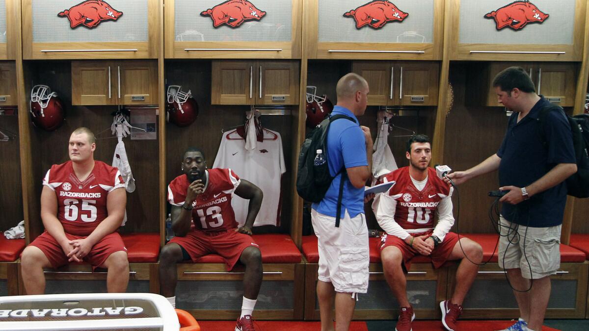 While Arkansas quarterback Brandon Allen (10) fields questions from reporters, senior center Mitch Smothers (65), all 322 pounds of him, sits patiently in the locker room with teammates.