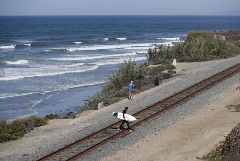 A surfer crosses the railroad tracks Tuesday along the bluffs in Del Mar.