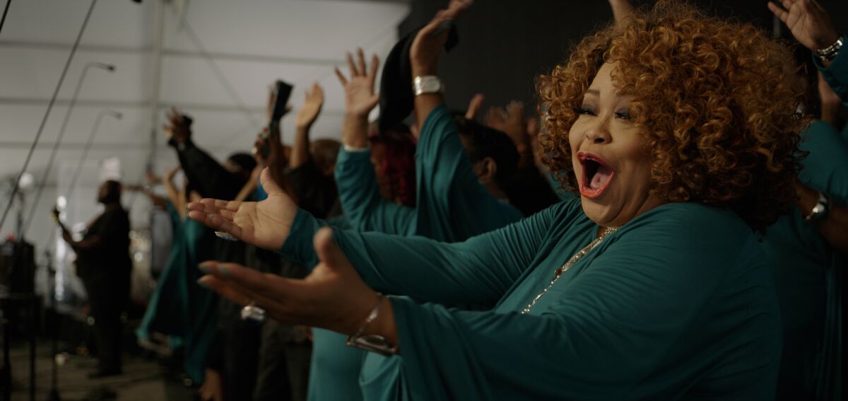 Closeup of a woman holding out both hands and singing among a choir.
