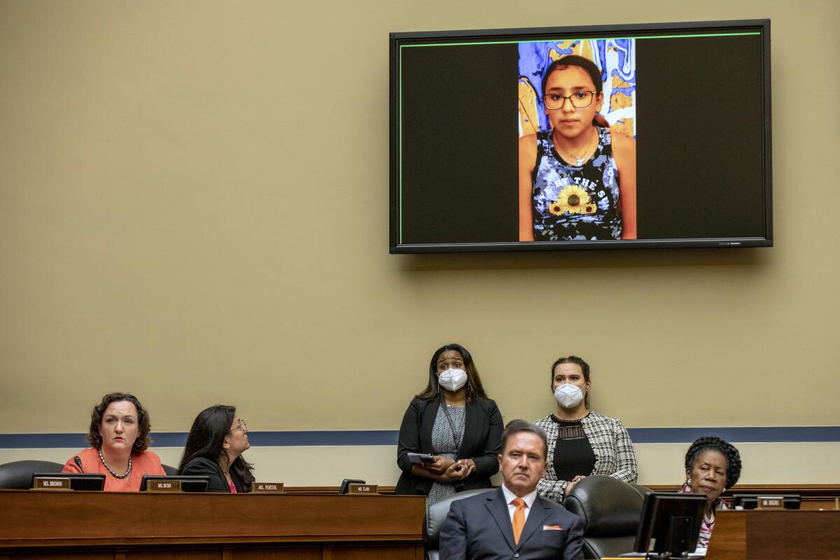 A girl appears on a screen above lawmakers and others sitting in a hearing room