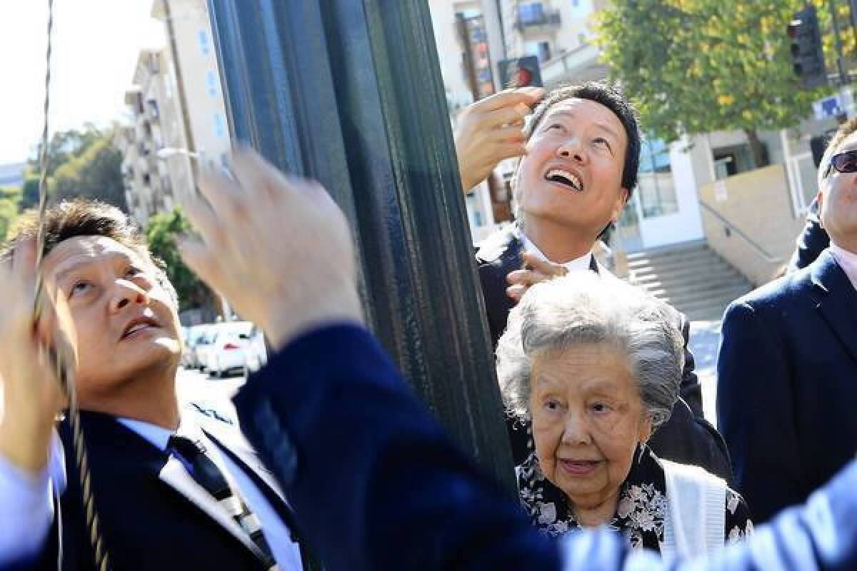 Dolores Wong, right, widow of Judge Delbert E. Wong, and sons Kent, right, and Marshall, left, pull down a velvet cloth to unveil a sign naming the Chinatown intersection of Ord and Hill streets for the former jurist.
