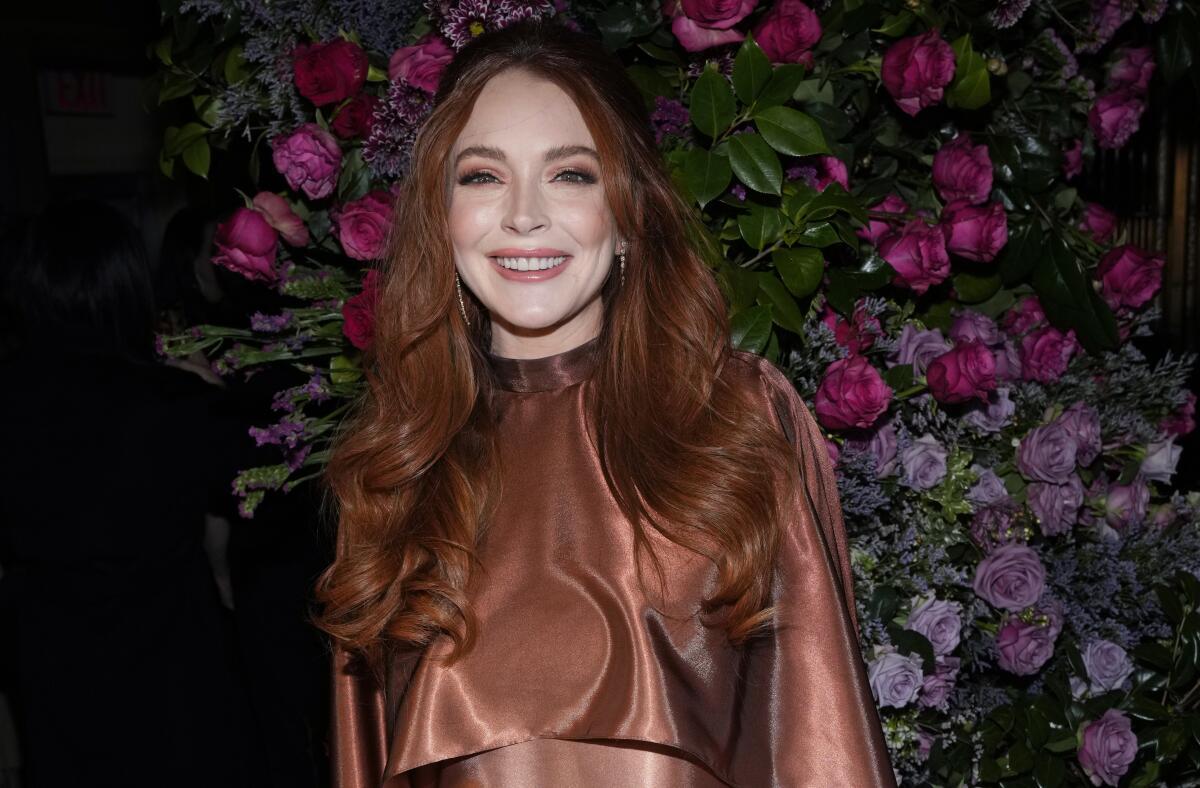 Lindsay Lohan smiles in a copper dress against a floral backdrop.