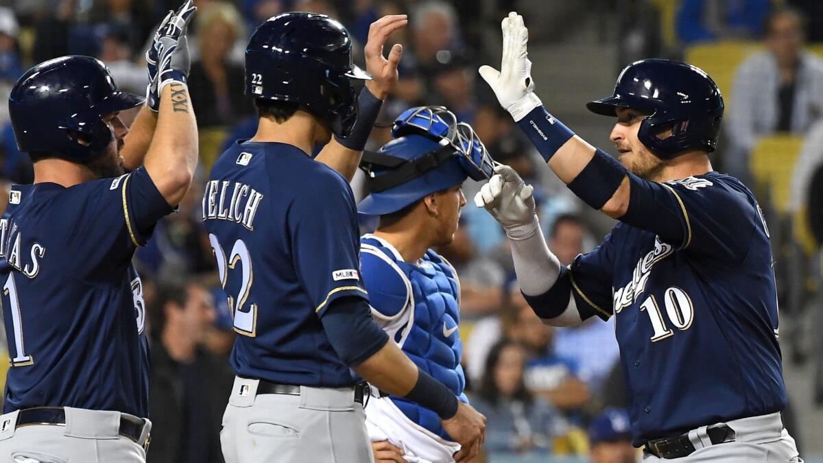 Austin Barnes of the Dodgers looks on as Yasmani Grandal (10) is greeted by Christian Yelich (22) and Mike Moustakas (11) of the Milwaukee Brewers after hitting a two-run home run in the fifth inning at Dodger Stadium.