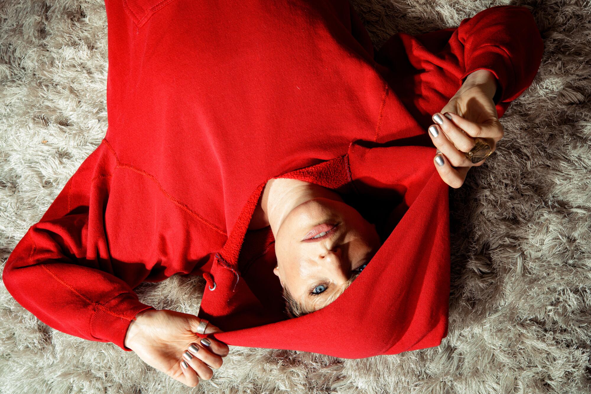 A woman in a red hoodie lying on a shag rug.