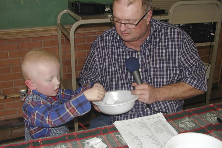 In a photo provided by Carolyn Plotts, Eric Kuhlman, 3, helps master of ceremonies Stan Miller draw names for the annual Norcator drawing held in Norcatur, Kan. For the 150 or so people who still call the rural hamlet home, the cancellation this year of the town's beloved Norcatur Christmas Drawing has shone a spotlight on a global coronavirus pandemic that has reached deep into rural America. (Carolyn Plotts via AP)