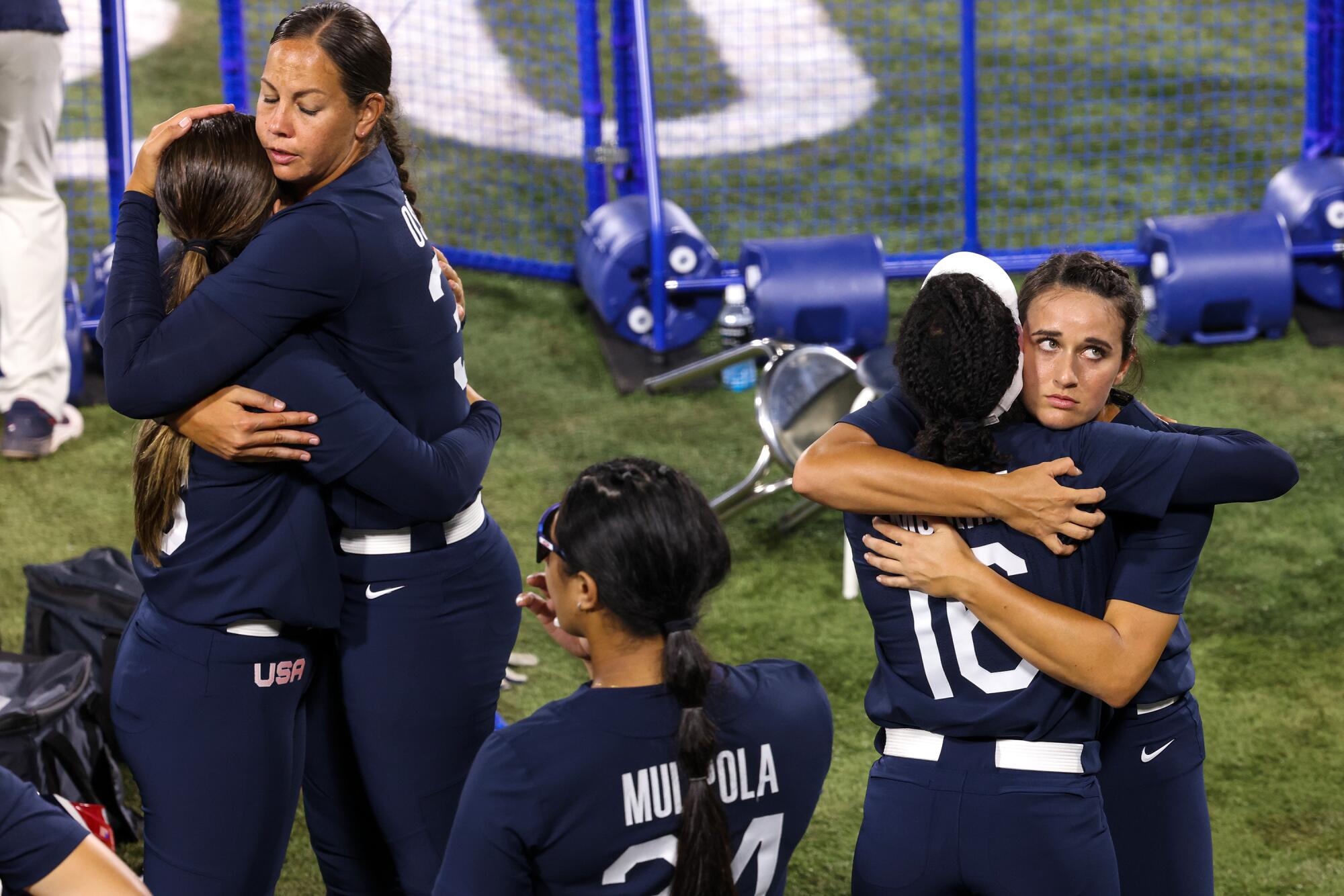 Women somberly stand on the field and hug.