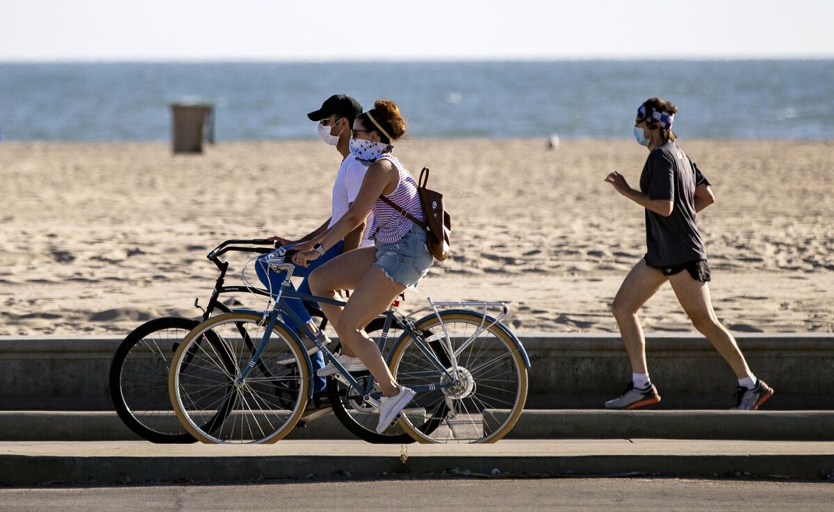 Bicyclists and a runner wear masks on the boardwalk in Santa Monica