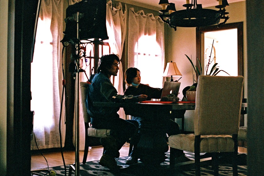Two people look at a laptop while sitting at a dining table.