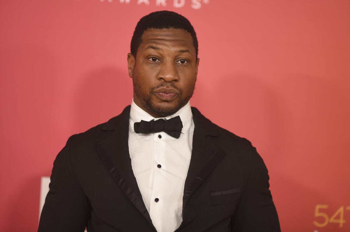 Jonathan Majors wearing a black tuxedo and bow tie against a pink background