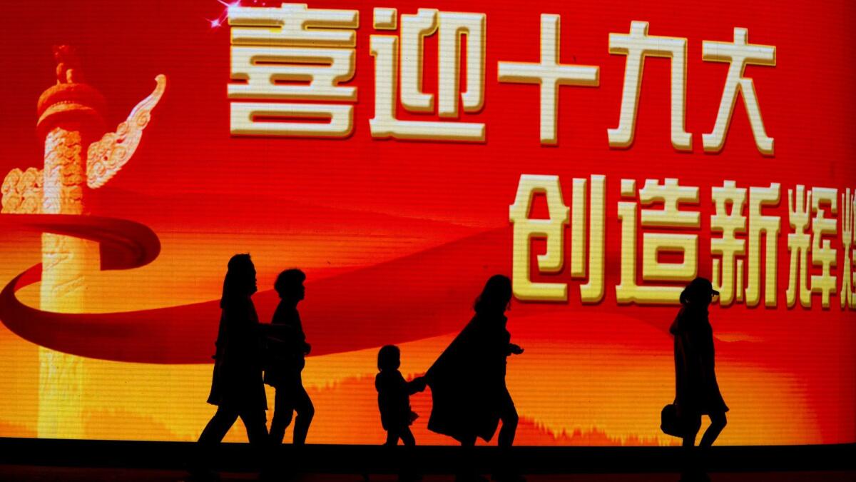 Shoppers pass by a slogan that reads, "Welcome the 19th party congress, create new glories" in Beijing on Oct. 15, 2017.