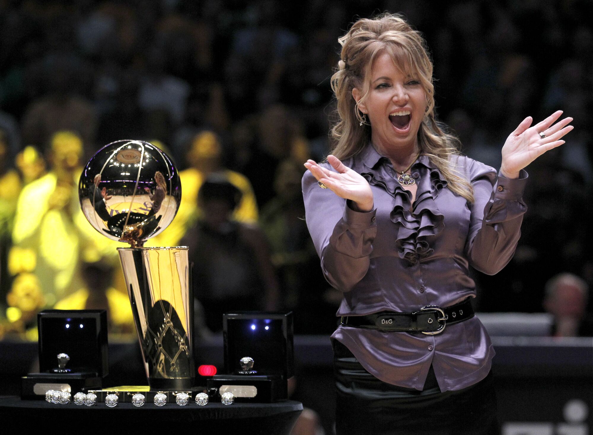A woman stands applauding next to the NBA Championship trophy