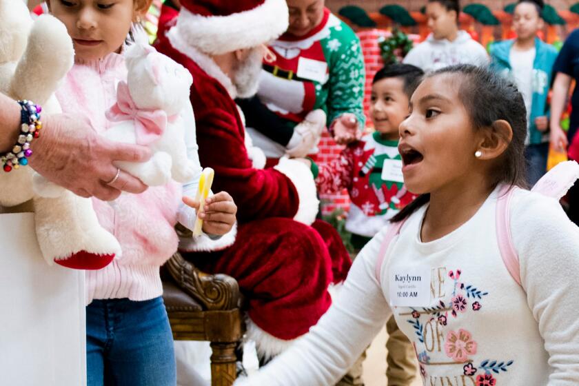 LENNOX CA DECEMBER 14, 2019 -- From left: After hugging Santa Claus, Giselle Palacios (5), left, and Kaylynn Palacios (7) get to pick a teddy bear to keep. Lennox Middle School hosts St. Margarets Centers 31st Annual Christmas Program for 500 prescreened families living at or below the poverty level. More than 400 volunteers provided a day of Christmas activities for families in need. (Klaudia Lech / For The Times)