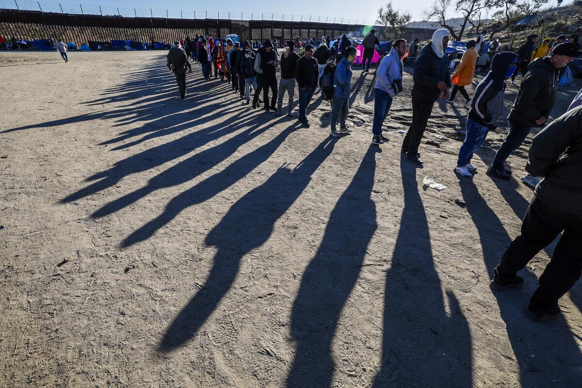Migrants line up for food provided by volunteers at a makeshift camp near the border wall in Jacumba, Calif.