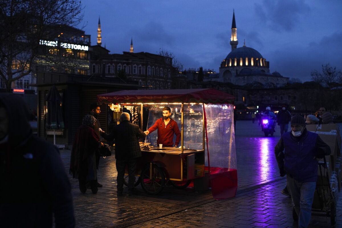 A roast chestnut seller talks to customers in Istanbul, Turkey, Thursday, Dec. 16, 2021. Turkey's Central Bank again cut a key interest rate Thursday despite soaring consumer prices that are making it difficult for people to buy food and other basic goods, sending the country's currency to record lows against the U.S. dollar. The bank's monetary policy committee said it is cutting the rate from 15% to 14%, though inflation is running at 21%, according to official data. (AP Photo/Francisco Seco)